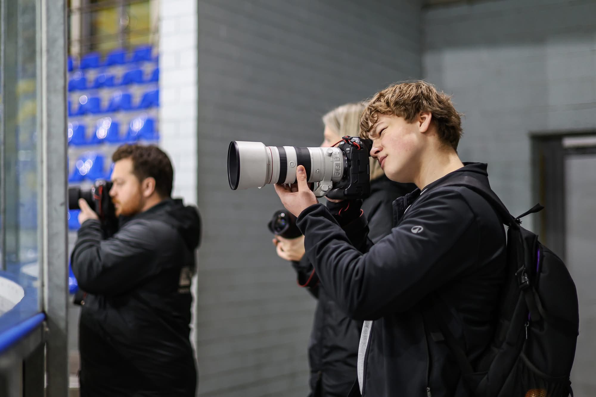 Gustavs Ruģelis fotografē hokeja spēli pie laukuma